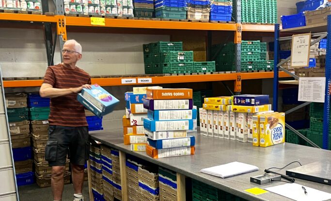 Male volunteer relocating stacks of cereal boxes from a work table to shelves