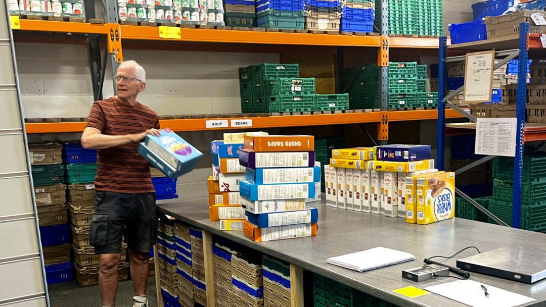 Male volunteer relocating stacks of cereal boxes from a work table to shelves