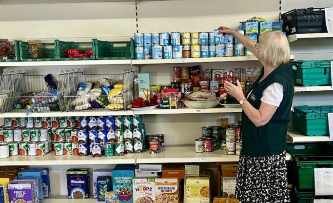 Lady stacking tins of food on shelving unti