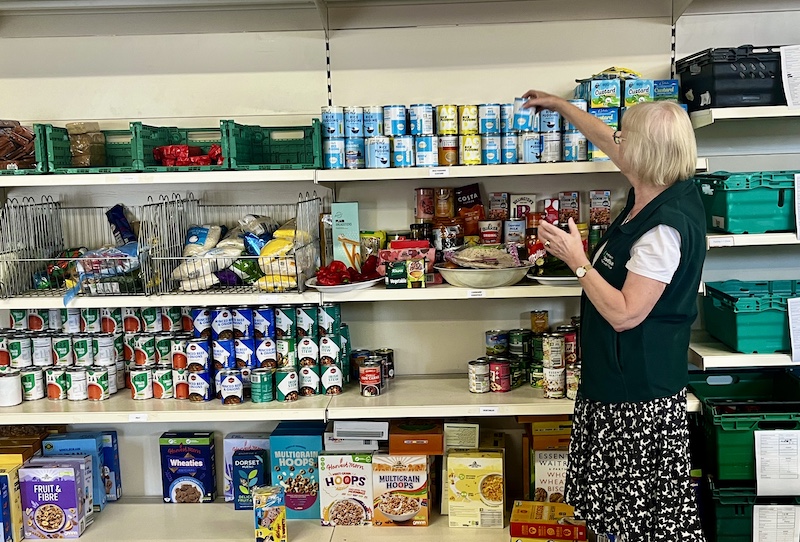Lady stacking tins of food on shelving unti